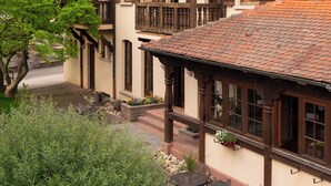 A traditional half-timbered building with a courtyard featuring outdoor seating and a tree. - Hôtel Au Heimbach (Lembach)