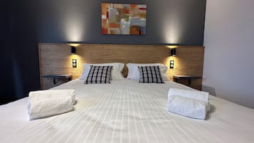Ein ordentlich bezogenes Bett mit gestreifter Bettwäsche, zwei Kissen und zwei Nachttische mit Wandleuchten.