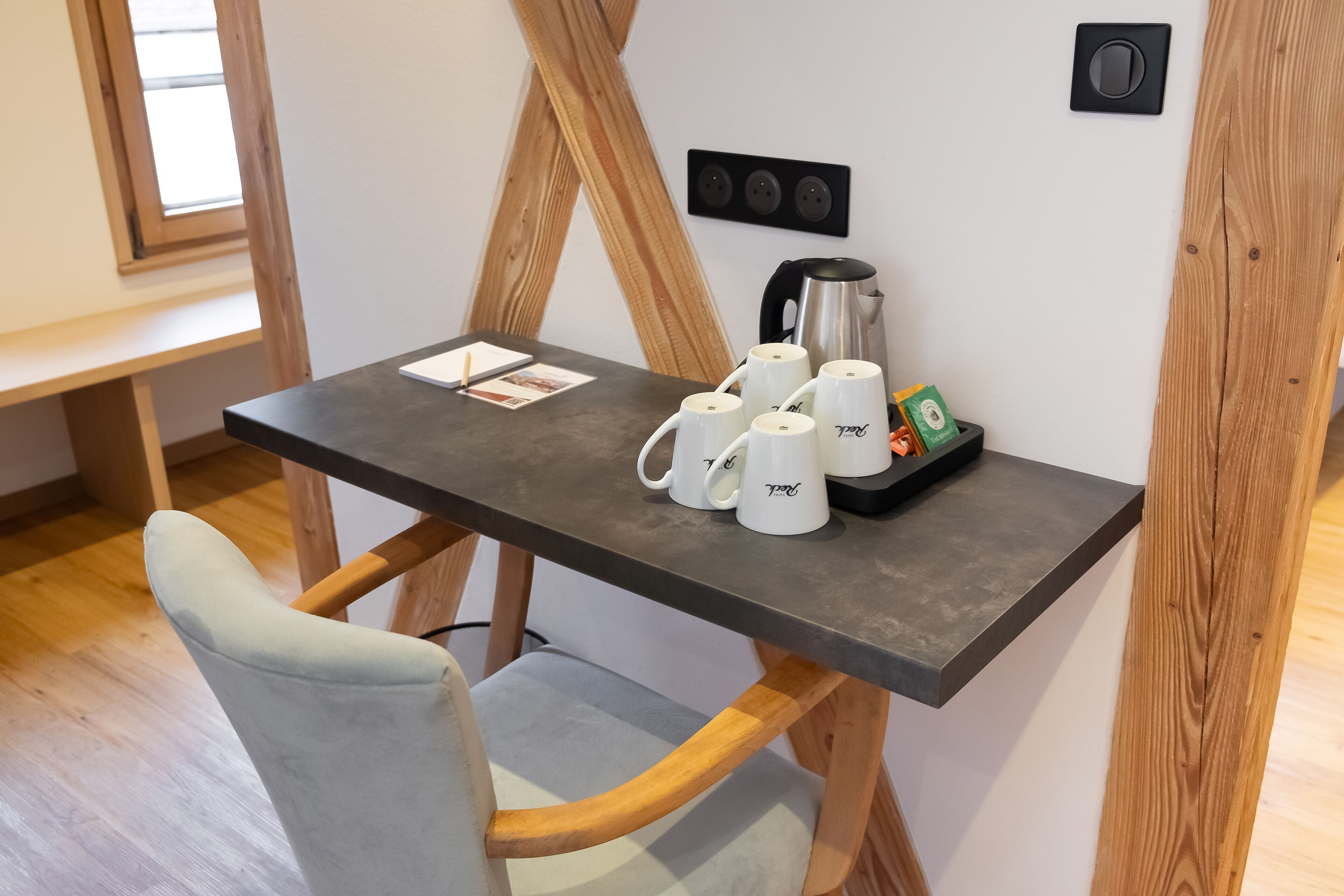 Ein kleiner Tisch mit einer Kaffeemaschine, vier weißen Tassen und einer Schale mit einer grünen Box.