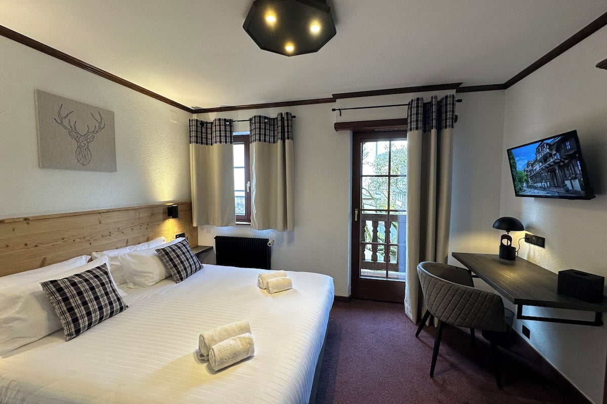 A hotel room with a large bed, a desk, a chair, a television, and a window with curtains.
