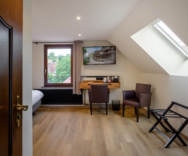 A compact room with a bed, a desk with a computer, two chairs, a radiator, a window with curtains, a painting, and a skylight. - Hôtel Au Heimbach (Lembach)