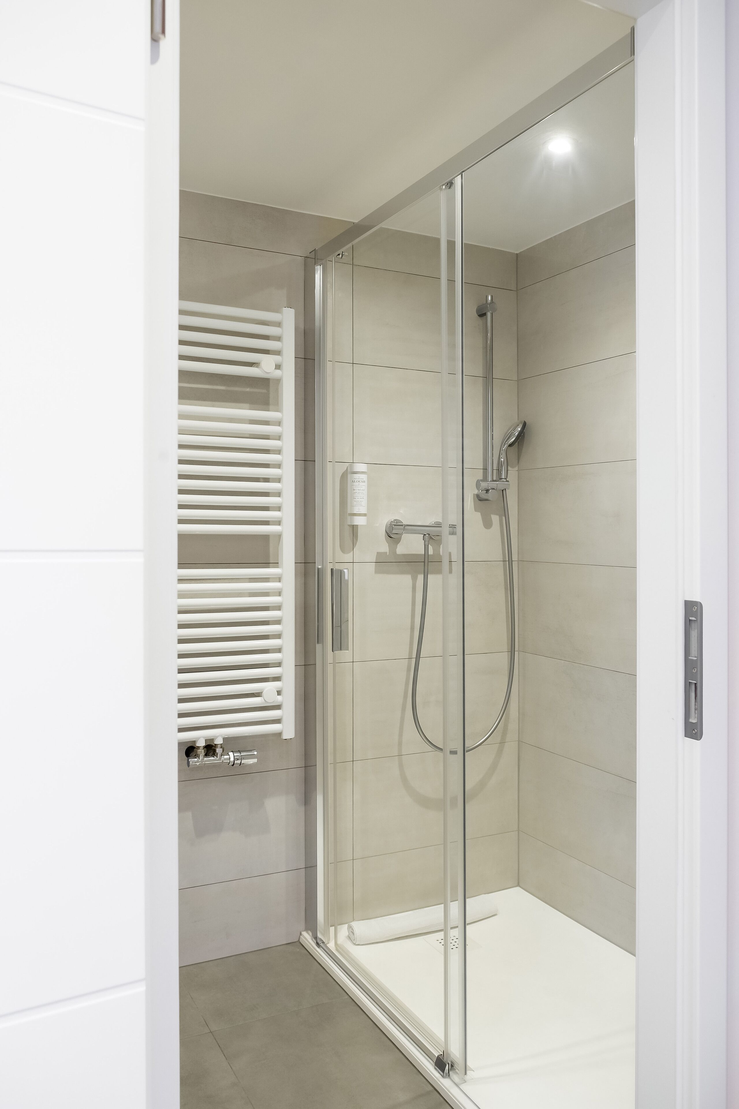 Una ducha moderna con puerta de vidrio, un perchero blanco y un panel de control.