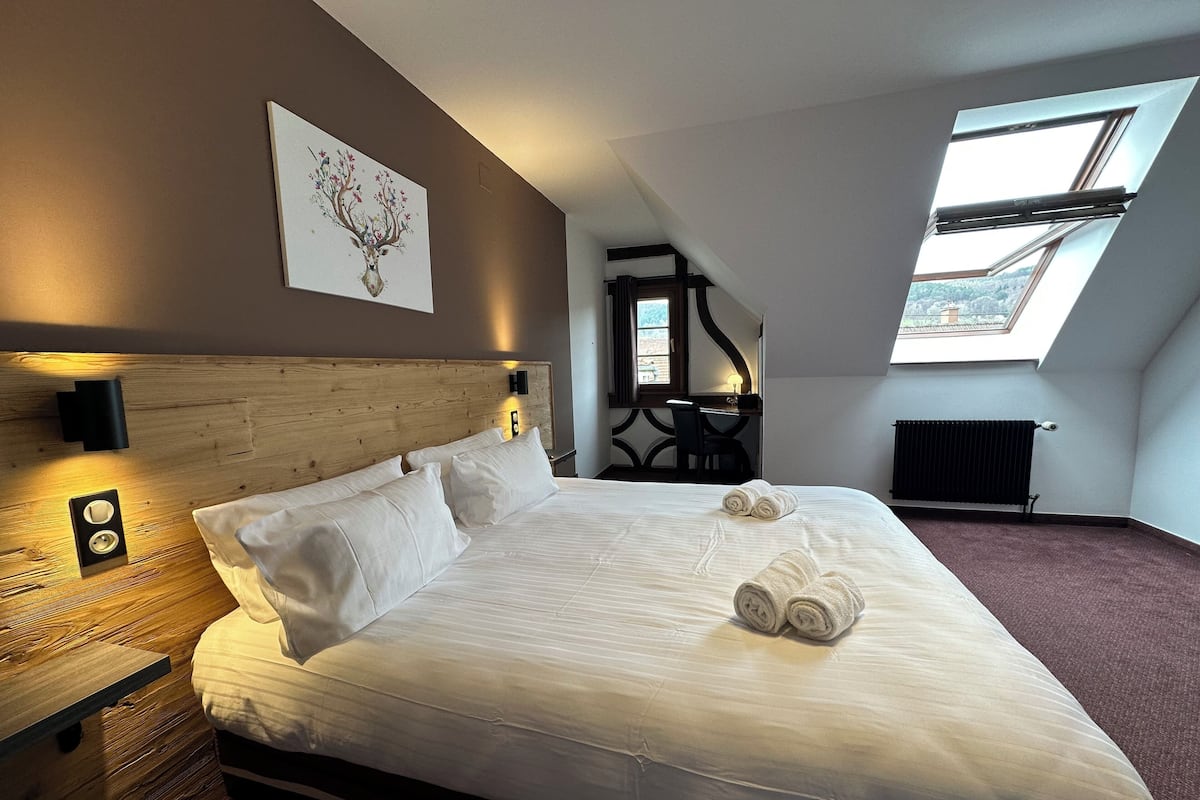 A bedroom with a large bed, a wooden headboard, a skylight, and a painting on the wall.