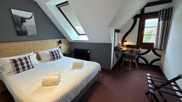 A bedroom with a large bed, a desk, a chair, a radiator, and a skylight.