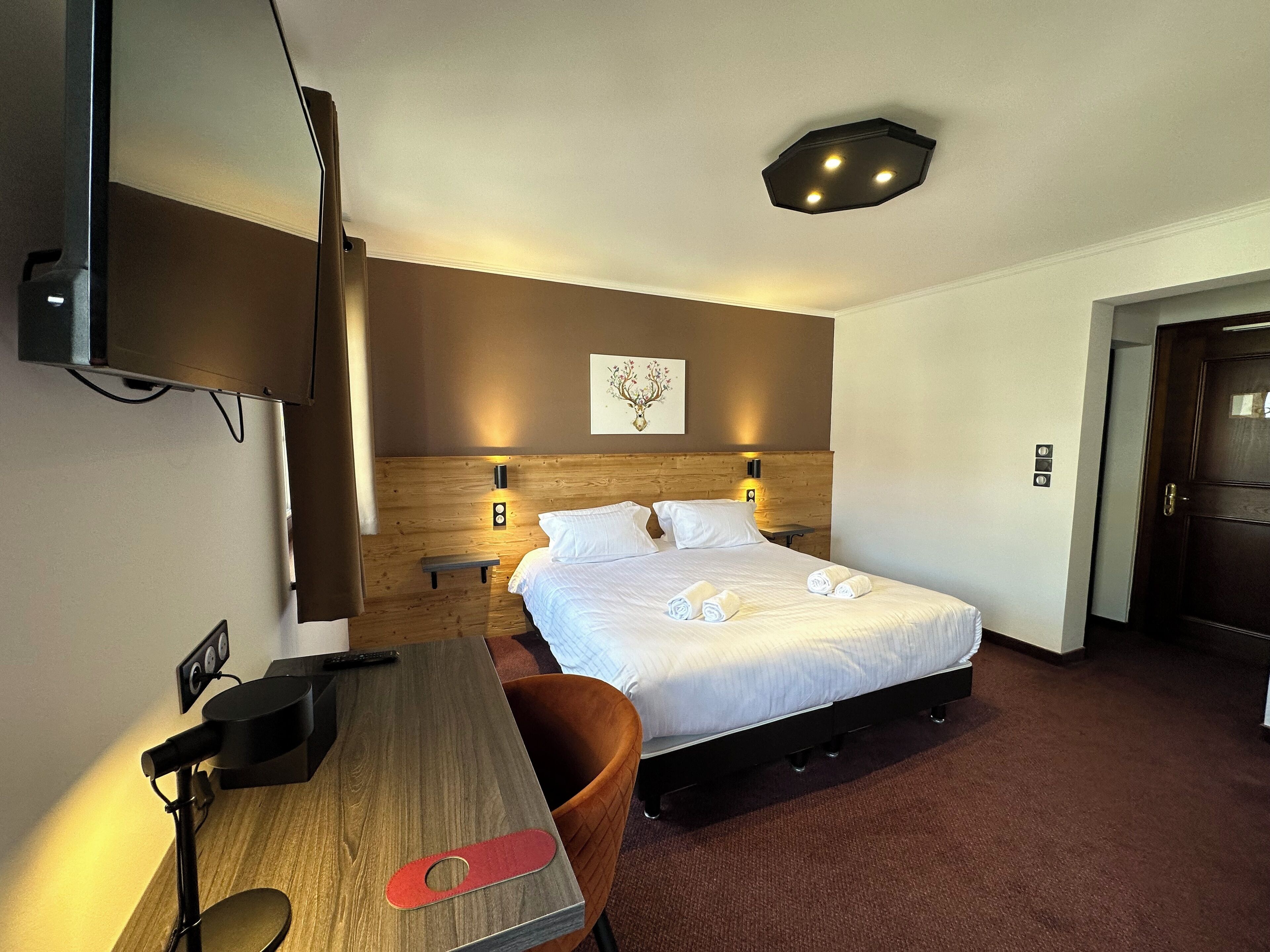 Une chambre d’hôtel avec un lit, un bureau, une chaise, une télévision et une porte.