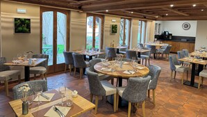 A restaurant with round tables, grey upholstered chairs, wooden flooring, and large windows. - Hôtel Au Heimbach (Lembach)