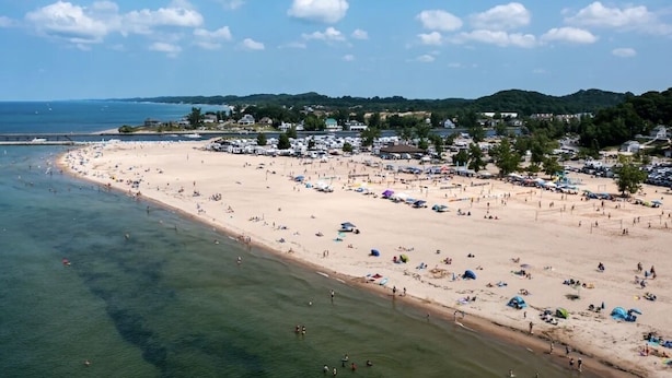 A beach with clear waters, a sandy shore, and a backdrop of hills and buildings.