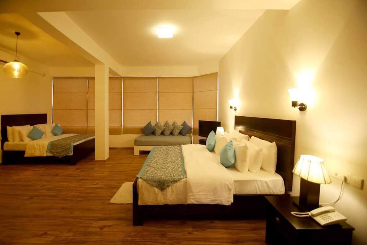 Una habitación de hotel con dos camas, un sofá, una mesita de noche con lámpara y teléfono.