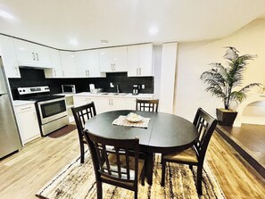 Una cocina moderna con armarios blancos, una encimera negra y un comedor con una mesa redonda y cuatro sillas.