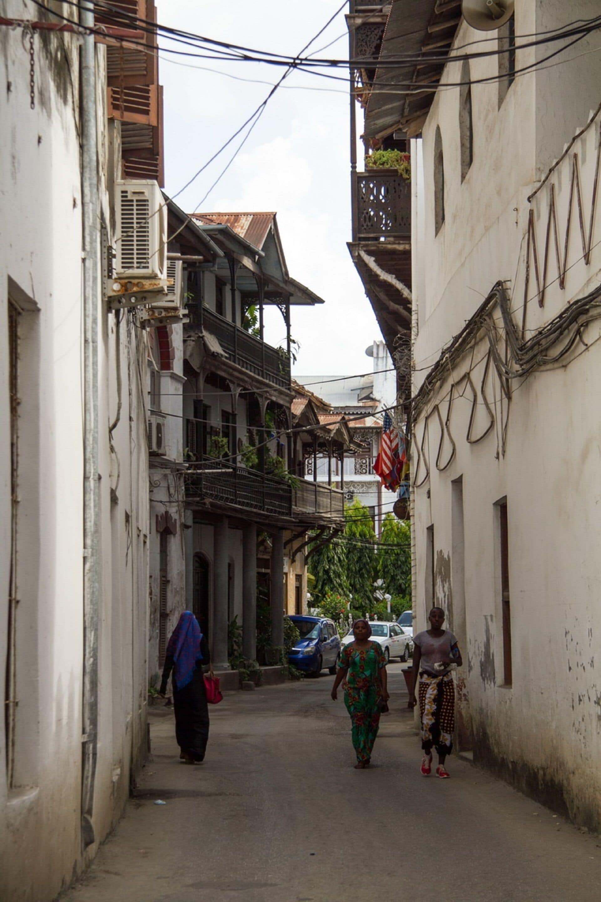 A narrow street with buildings on either side, featuring balconies and air conditioning units.