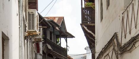 A narrow street with buildings on either side, featuring balconies and air conditioning units.