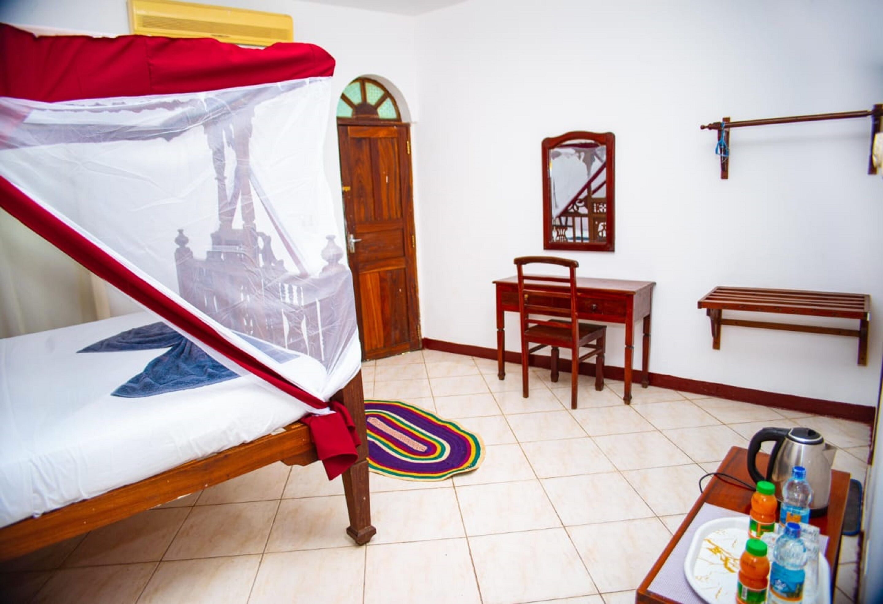 A room with a bed, a chair, a table with bottles, a kettle, and a mirror.