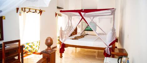 A room with a bed covered by a mosquito net, a small table with bottles, and a chair.