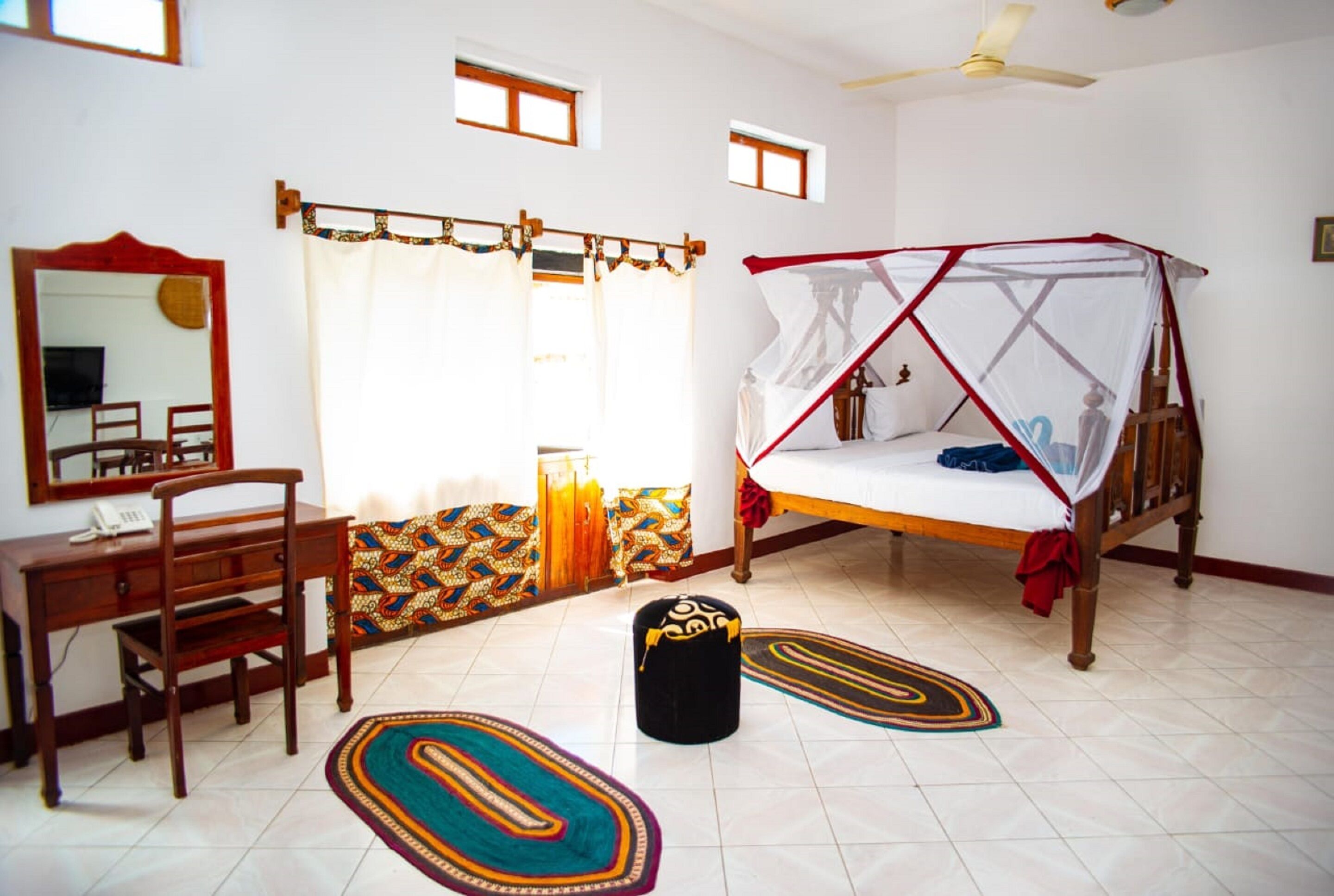 A bedroom with a bed, a desk, a chair, a mirror, and a ceiling fan.