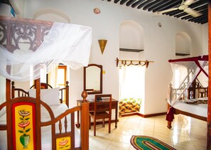 A room with a bed under a canopy, a desk with a chair, a mirror, and a colorful rug. - La Neisha Hotel Zanzibar (Zanzibar Town)