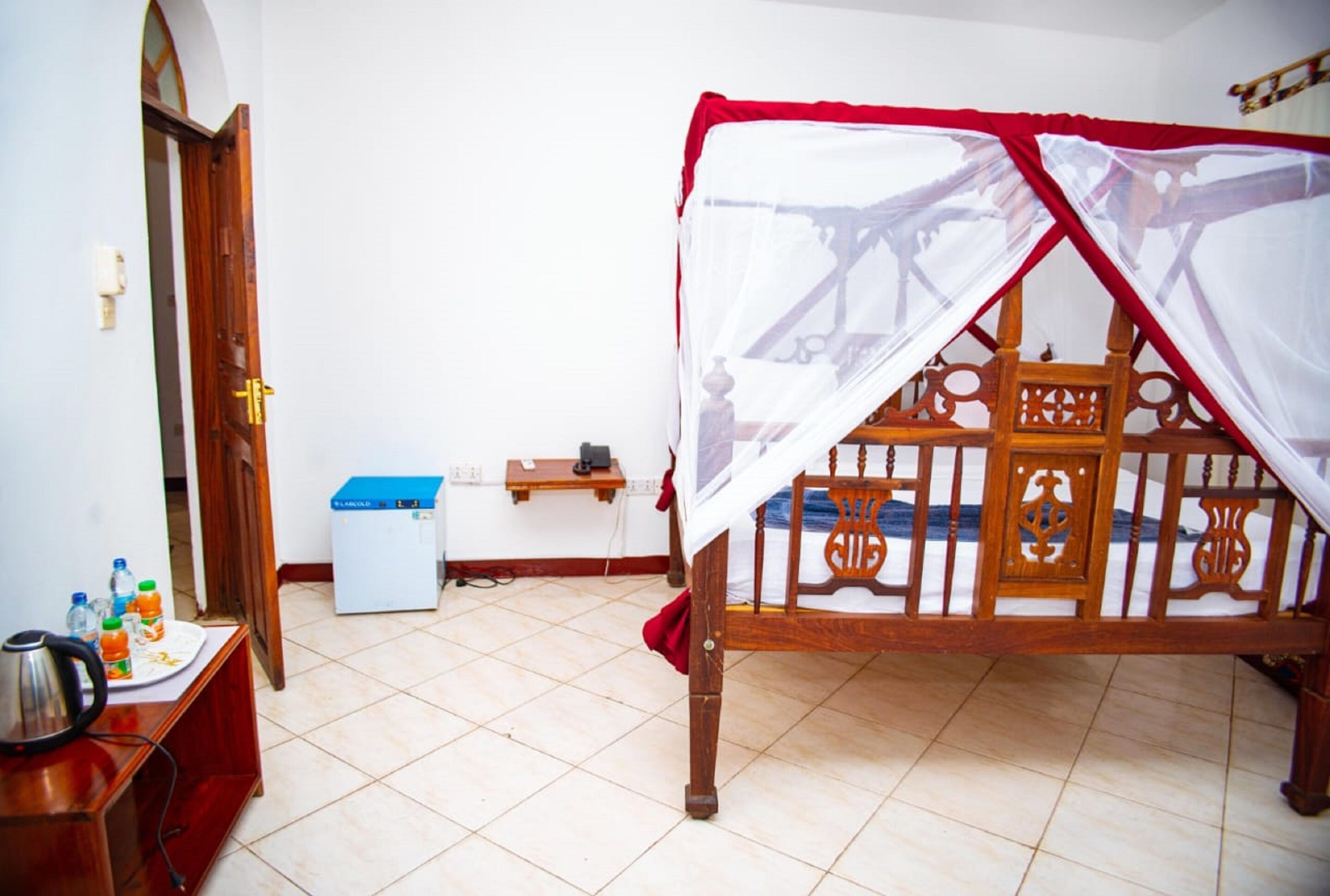 A bedroom with a wooden bed, a small desk with a kettle, a trash bin, and a blue storage box.