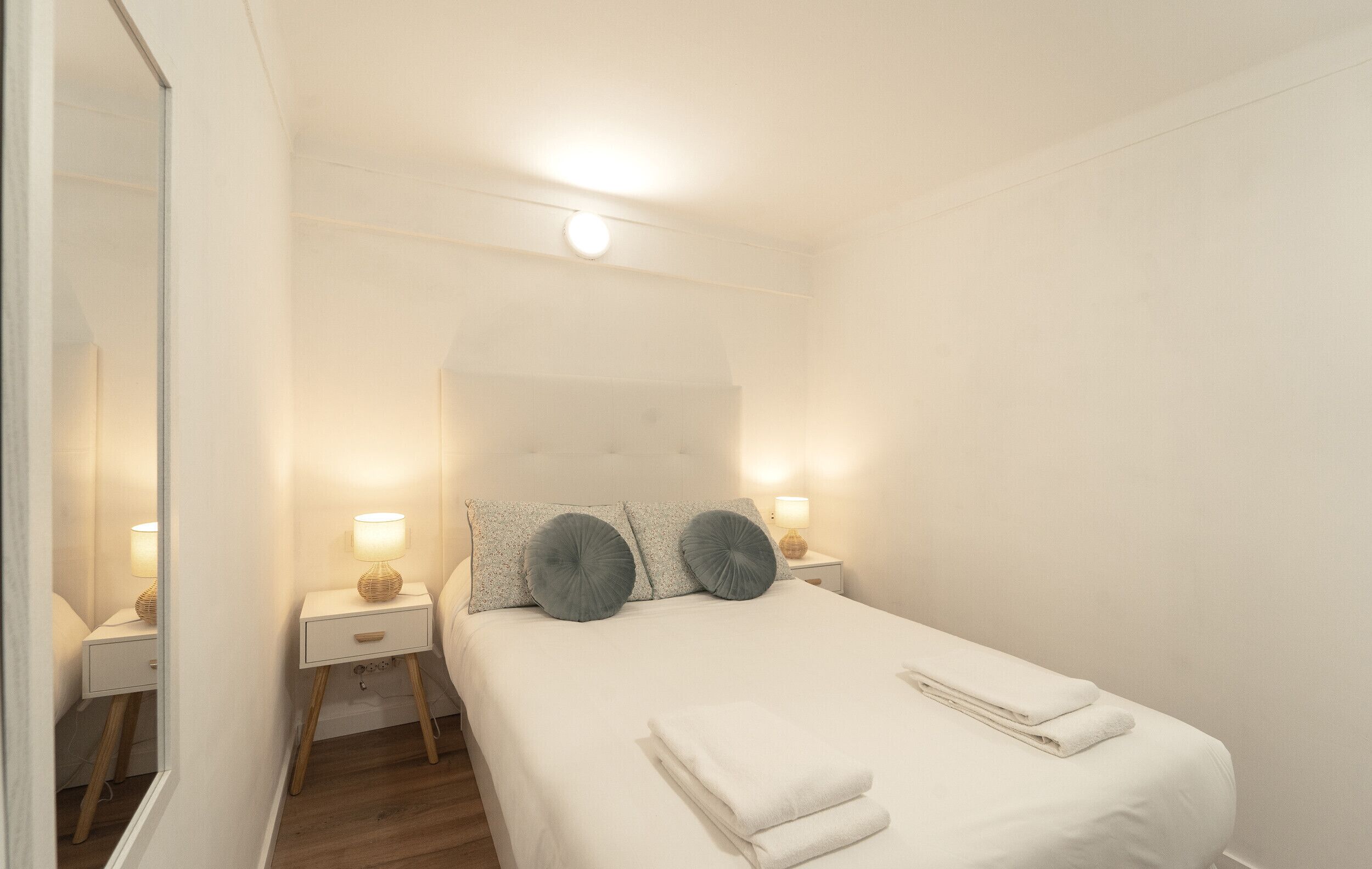 A neatly arranged bedroom with a bed, bedside tables, and a mirror.