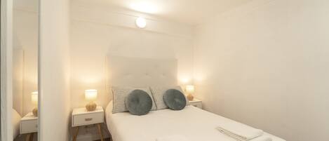 A neatly arranged bedroom with a bed, bedside tables, and a mirror.