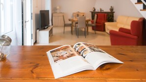 A magazine open on a wooden table in a living room with a dining area, red and beige sofas, and a staircase. - WELCS CASA 089 EMP cerca del mar (Empuriabrava)