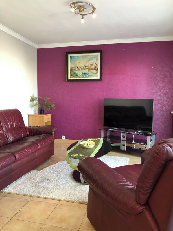 Una sala de estar con una pared morada, un televisor de pantalla plana, un sofá de cuero, una mesita de centro y un cuadro enmarcado.