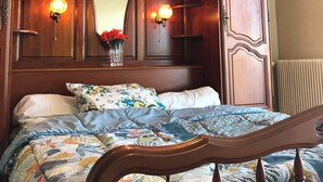 A bedroom with a wooden bed frame, a large mirror, and two wall-mounted lamps.
