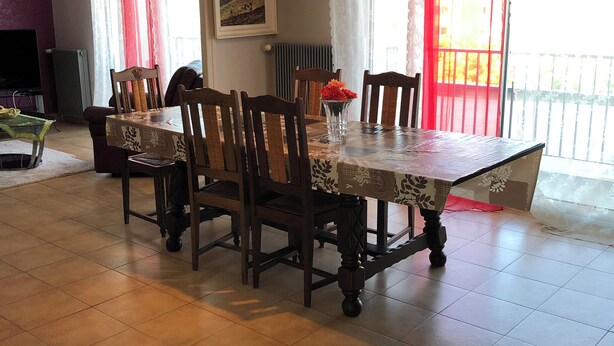 A dining area with a table and chairs, a painting on the wall, and a view of the outside balcony.
