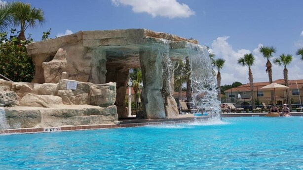 Una piscina amb cascada, envoltada de palmeres i una estructura de pedra.