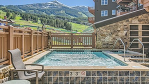 A pool area with a view of mountains, wooden deck chairs, and a stone wall.