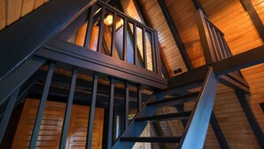 A wooden staircase with metal railings leading to a lofted area with a sloped ceiling and exposed beams.