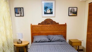 A bedroom with a large bed, two bedside tables, a wooden headboard, and framed pictures on the walls.