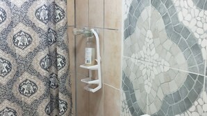A bathroom with a shower, patterned curtain, tiled walls, and a toilet.