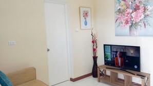 A living room with a television on a wooden stand, a door, and a painting of flowers on the wall.