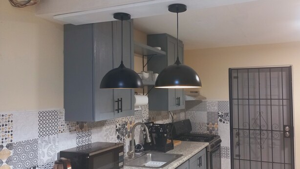A kitchen with grey cabinets, a black countertop, a sink, a stove, and two pendant lights.