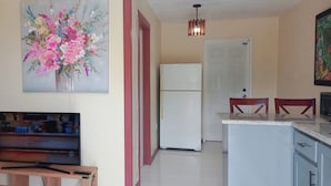 A kitchen with a refrigerator, a dining area with chairs, a TV, and a painting on the wall.