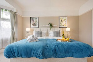 Quarto de hotel com uma cama grande, duas mesas de cabeceira, uma janela com cortinas e obras de arte nas paredes.