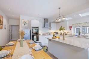 A modern kitchen with white cabinetry, a central island, and a dining area set for six. - Elegant House • Central Location • Sleeps 8 • Free Parking • Fast Wifi • VirginTV • By Yoko Property (Northampton)