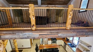 A spacious loft with a high ceiling, exposed wooden beams, a dining area with a wooden table and chairs, and a cozy seating area with a brown sofa.