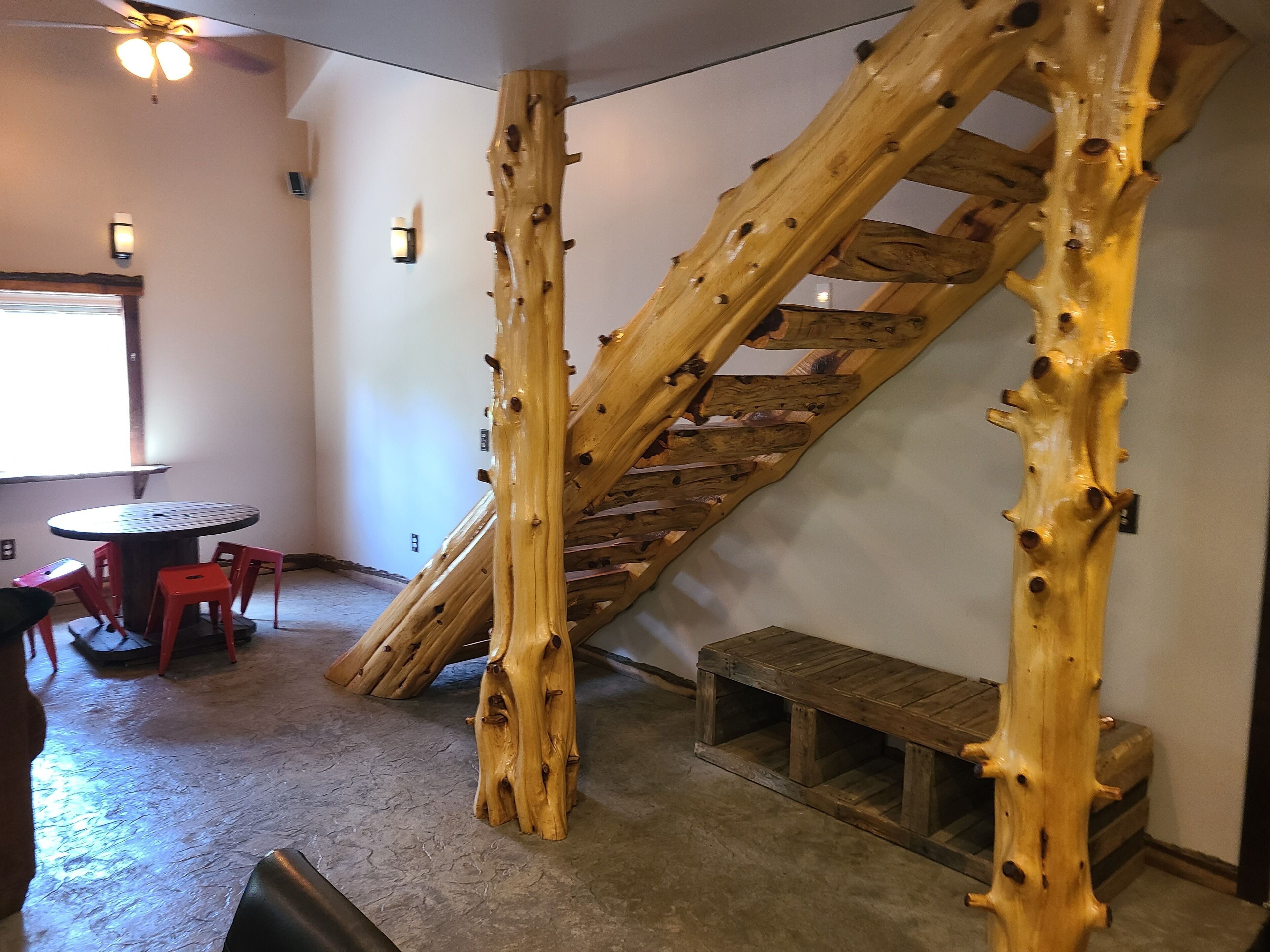 Una habitación con una escalera de madera, una mesa redonda con sillas y un banco.