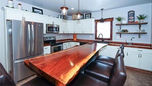 A modern kitchen with white cabinets, stainless steel appliances, a wooden island, and a bar area.