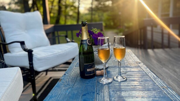 Eine Champagnerflasche und zwei Gläser auf einem Holztisch im Freien.
