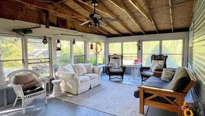 Ein Wintergarten mit Deckenventilator, Korbmöbeln und großen Fenstern, die einen Blick ins Freie bieten.