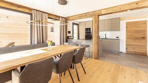 Ein moderner Essbereich mit Holztisch und -stühlen, einer Hängeleuchte und Blick in die Küche.