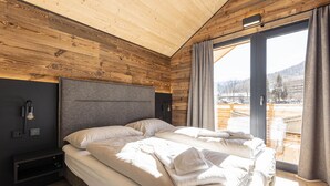 Ein modernes Schlafzimmer mit einem großen Bett, Holzboden und Blick auf eine verschneite Landschaft.
