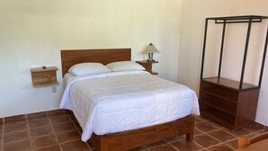 A bedroom with a wooden bed, white bedding, a nightstand with a lamp, and a wooden shelf. - POSADA CAMPESTRE XICOTEPEC (Xicotepec)