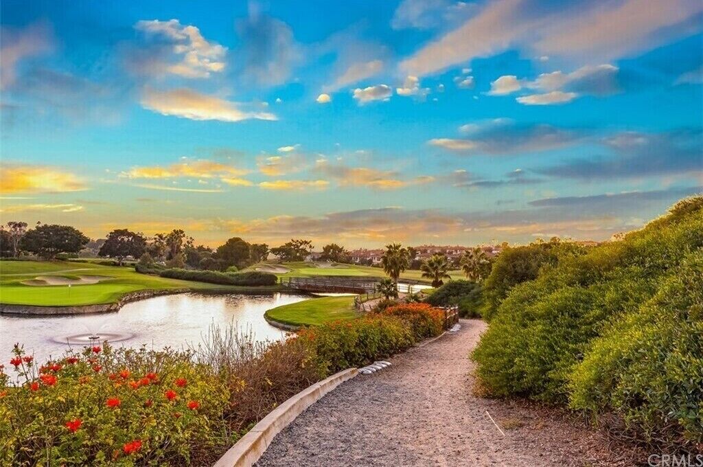 Un parcours de golf avec un étang, un sentier pédestre et une vue sur une ville au loin.