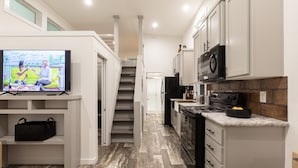 A compact kitchen with white cabinets, a black microwave, and a stove. A television is mounted on the wall, and a staircase leads to another level. - Oceans RV Resort (Holly Ridge)