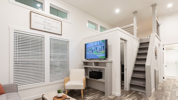 A modern living room with a television, a sofa, a coffee table, and a staircase. - Oceans RV Resort (Holly Ridge)