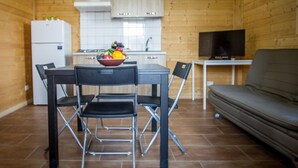 Cocina compacta con refrigerador, lavamanos y estufa. Se observa una mesa de comedor con sillas y un televisor sobre un mueble.
