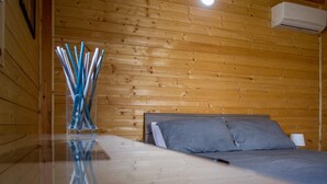 Un dormitorio de cabaña de madera con una cama, una mesita de noche y un aire acondicionado de pared.