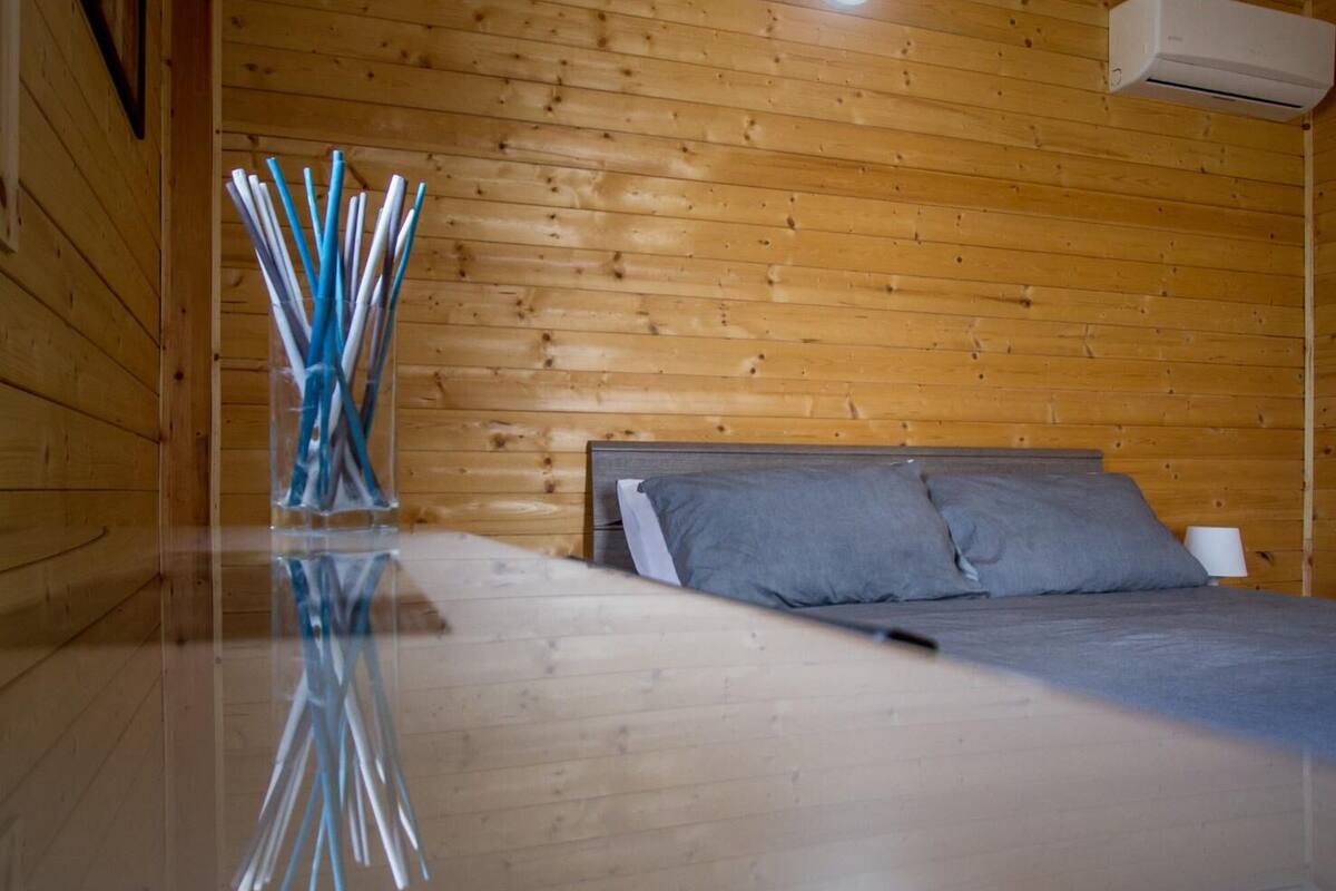 Un dormitorio de cabaña de madera con una cama, una mesita de noche y un aire acondicionado de pared.